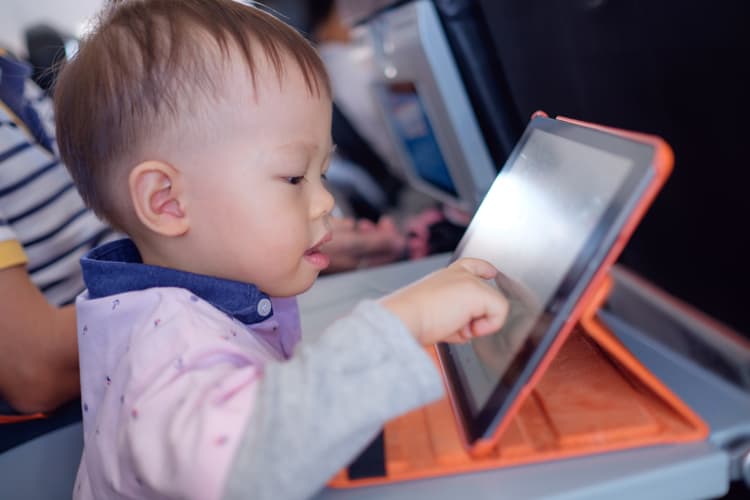 {Updated} 14 Tips For Stress-Free Flying With Babies And Toddlers 11 Child Playing On Ipad In Airplane For Stress-Free Flying With Babies And Toddlers