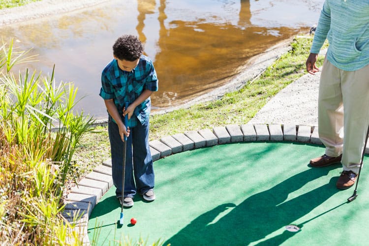 child playing mini golf with father