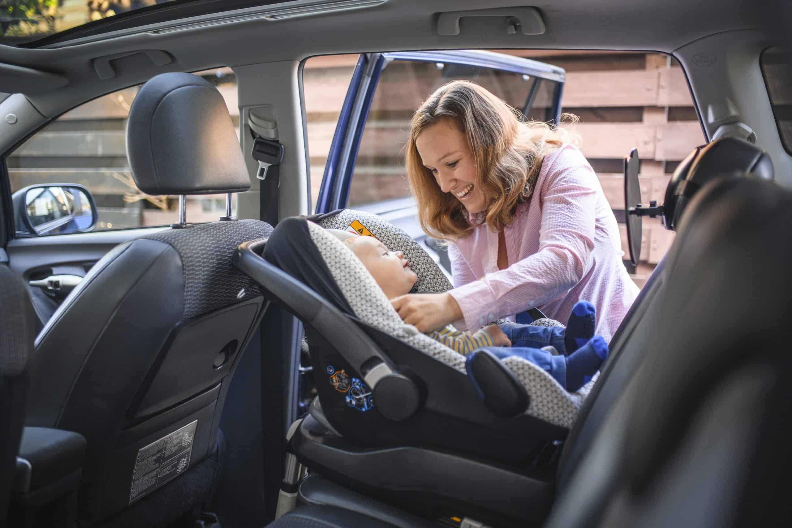 Mother securing a child in a car seat inside a vehicle.
