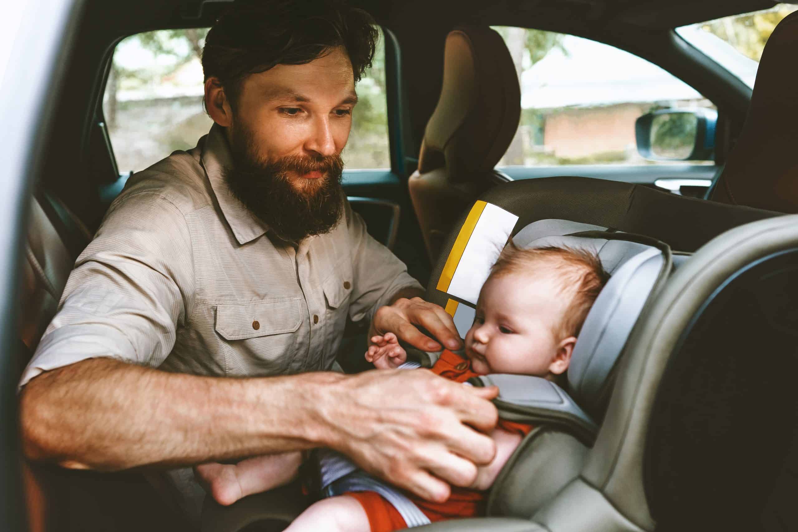 Father securing child in car seat in vehicle for safety.