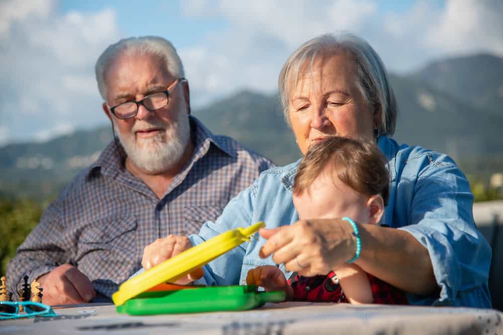 Family with grandparents and young child playing with colorful toys outdoors.