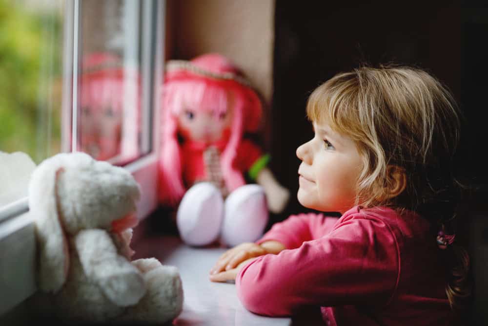 Young girl with teddy bear looking out window on rainy day in Wisconsin Dells.