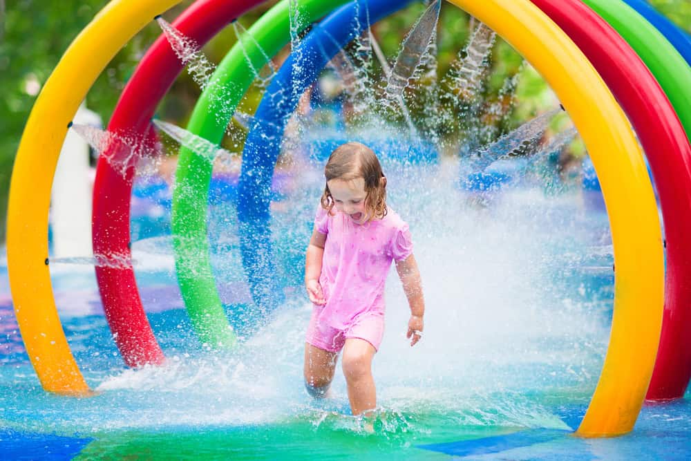 Child playing in water park with colorful water arches.