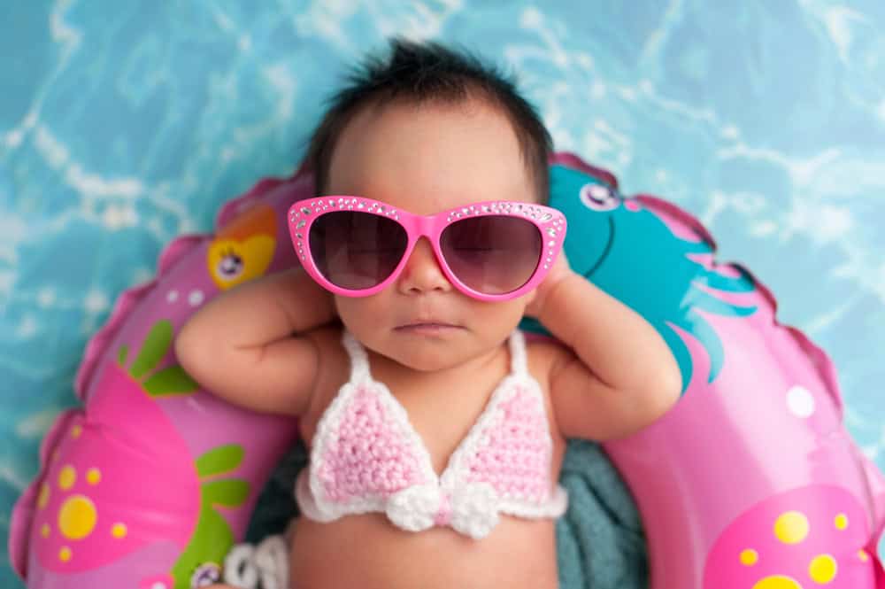 Baby in pink sunglasses and swim diaper relaxing in pool float.