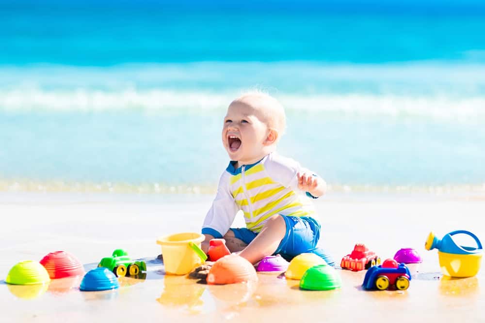 Bright baby playing with beach toys on Waikiki shoreline, enjoying a family vacation with baby gear.