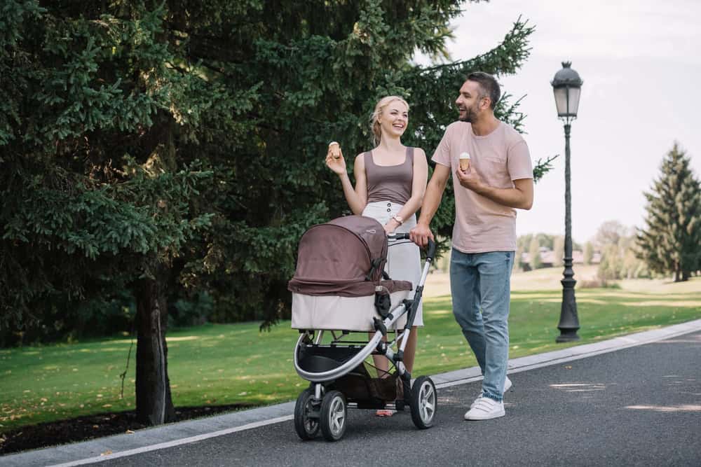 Comfortable parents walking with baby stroller in park, outdoor family activity, baby gear rental, p.