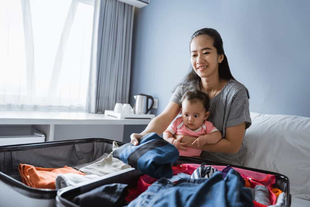 Packing and organizing baby gear in a suitcase for travel with a smiling mother and her baby.