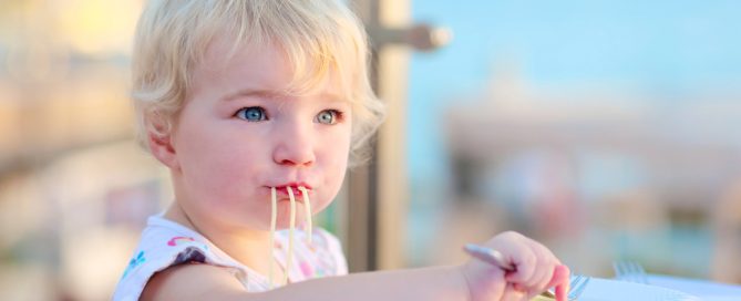 Young Child Eating Spaghetti Outdoors With Ocean View In Background.