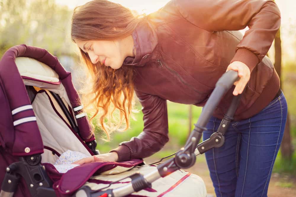 A woman adjusting a baby stroller outdoors in a park setting.