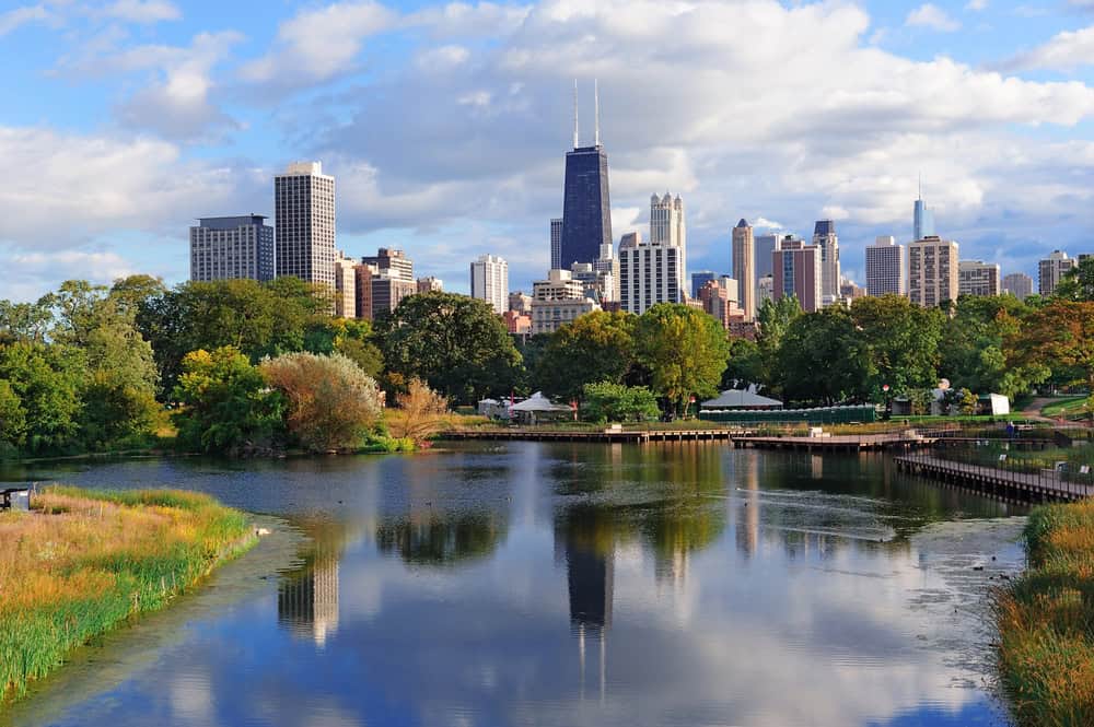 Chicago skyline with river and green park in foreground, sunny day with clouds.