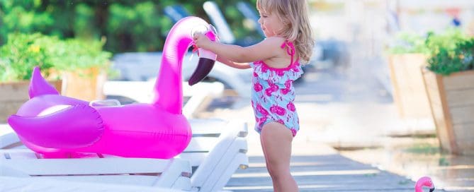 Young Girl Playing With A Pink Flamingo Pool Float On A Sunny Deck.