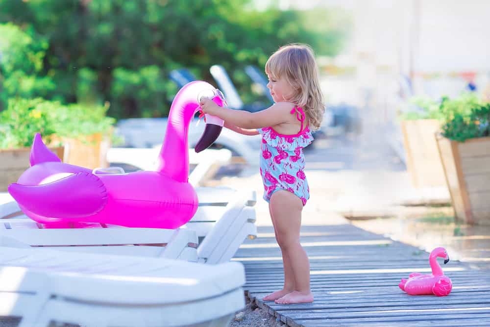 Young girl playing with a pink flamingo pool float on a sunny deck.