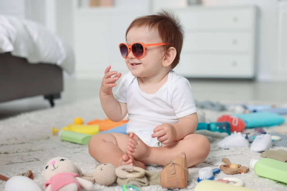 Cute toddler wearing sunglasses playing with toys on the floor.