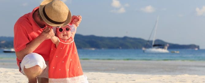 Parent And Toddler Enjoying A Beach Day With Sunglasses And Sun Hat.