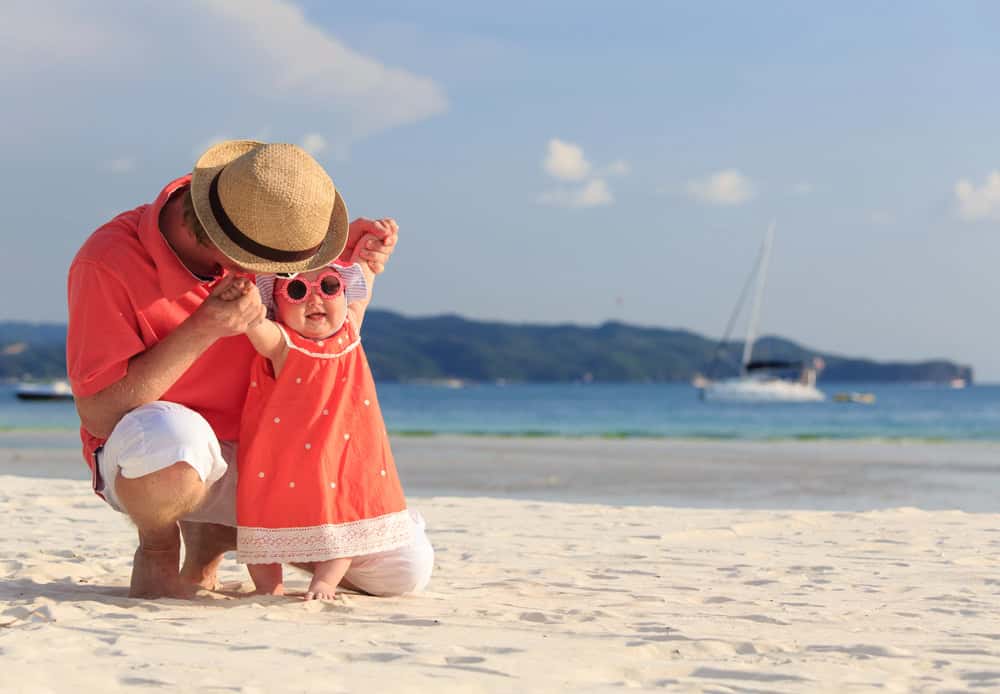 Parent and toddler enjoying a beach day with sunglasses and sun hat.