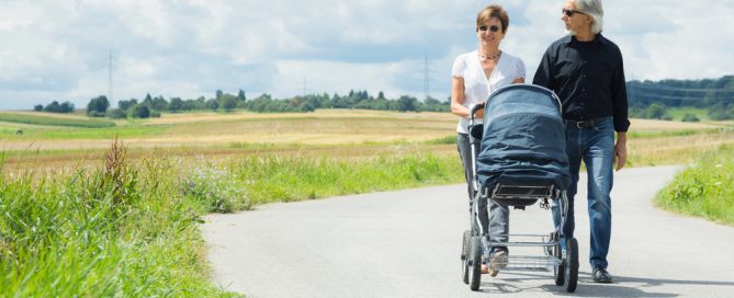 Elderly Couple Walking Outdoors With A Baby Stroller On A Sunny Day.
