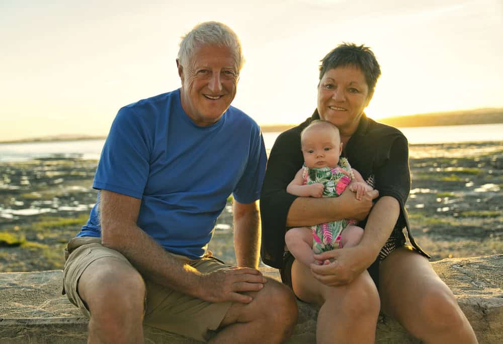Family enjoying a beach sunset with baby, grandparents, and mother.