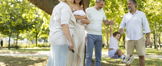 Family Enjoying A Day At The Park With A Pregnant Woman And A Young Girl On A Swing.
