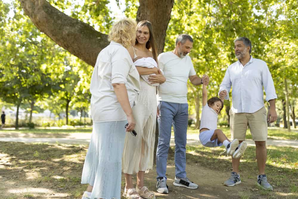 Family enjoying a day at the park with a pregnant woman and a young girl on a swing.