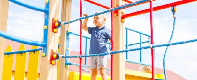 Child Playing On Colorful Outdoor Playground Equipment With Climbing Ropes And Slides.