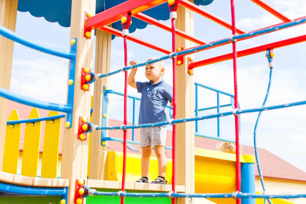 Child playing on colorful outdoor playground equipment with climbing ropes and slides.