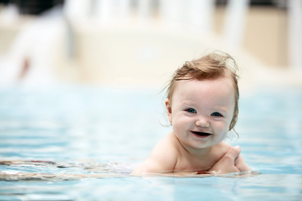 Smiling baby enjoying swimming in a pool with clear water.