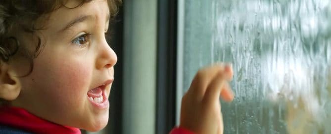 Child Looking Out A Rainy Window With Excitement And Curiosity.
