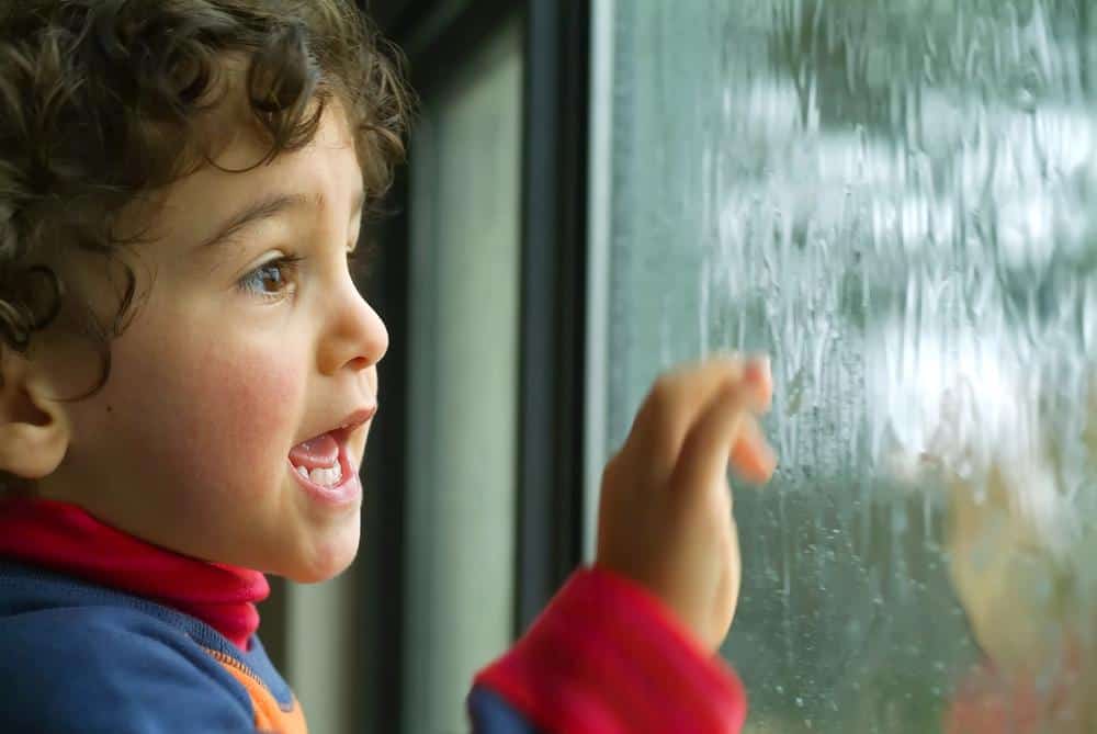 Child looking out a rainy window with excitement and curiosity.