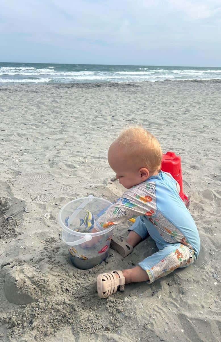 Baby playing with sand and toys on the beach during daytime.