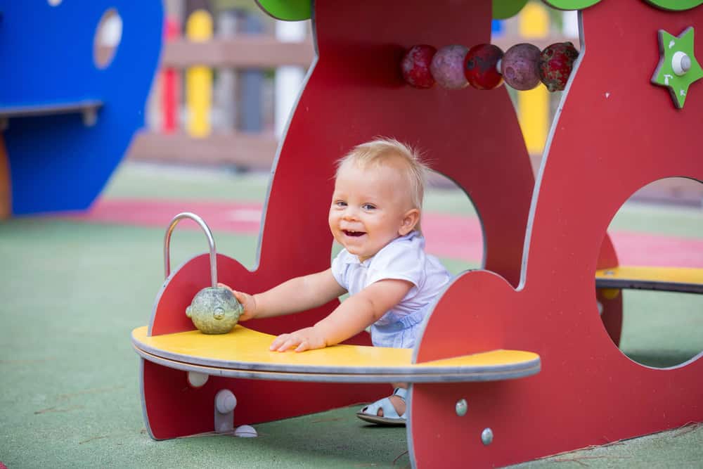 Baby playing on colorful playground equipment with a smile.