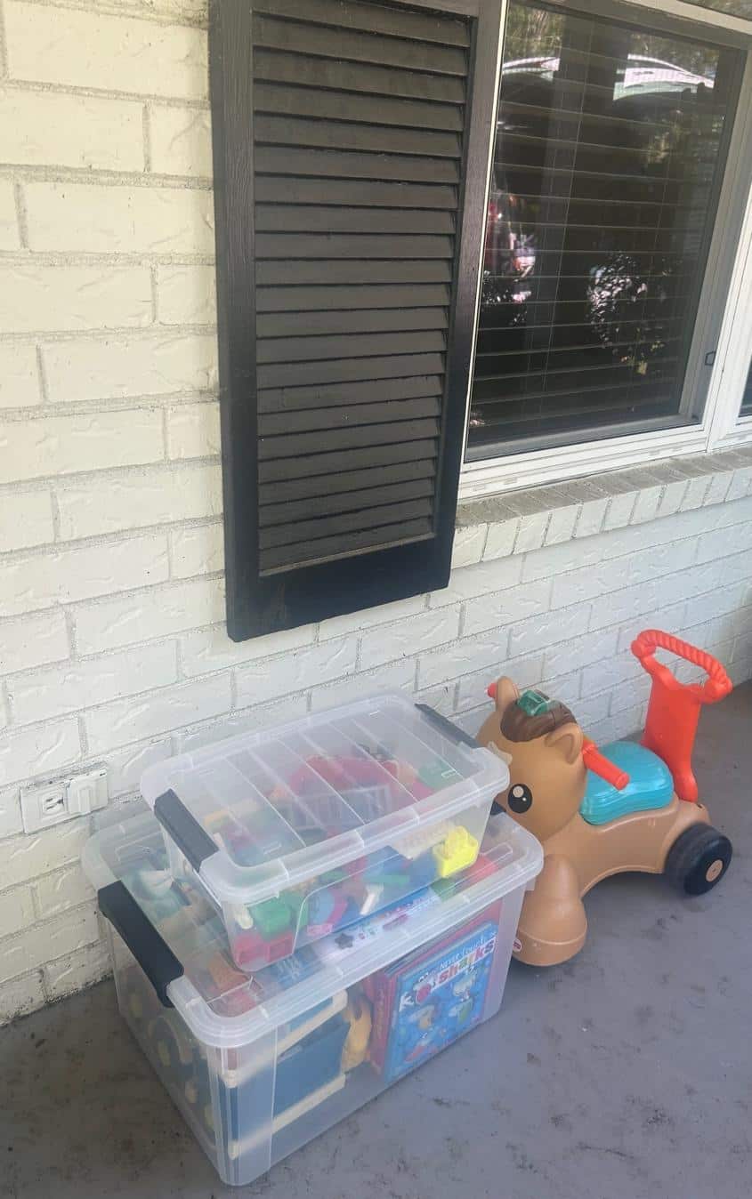 Child's toy ride-on car and storage bins outside a house.