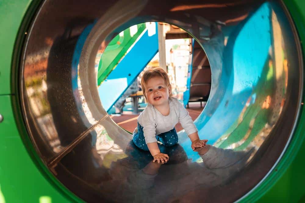 Baby crawling through colorful playground tunnel for kids.