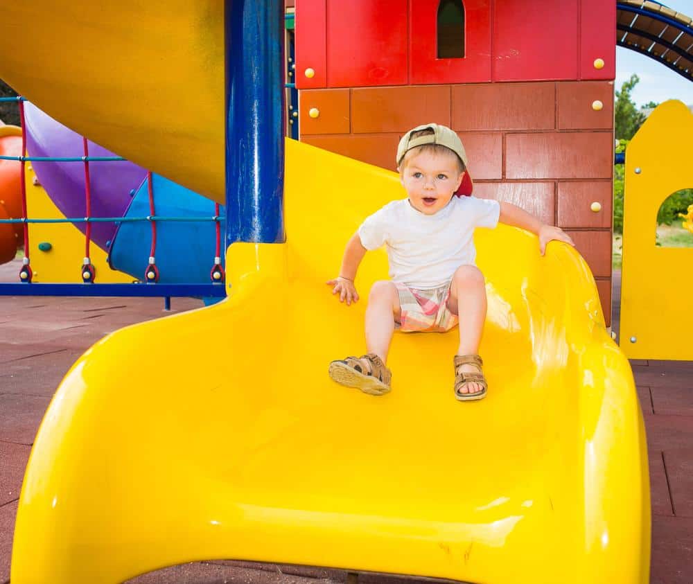 Young boy enjoying a yellow playground slide at the park.