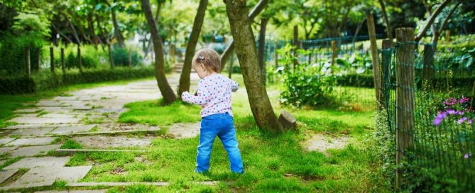 Child Exploring A Lush Green Garden With Trees And Flowers.