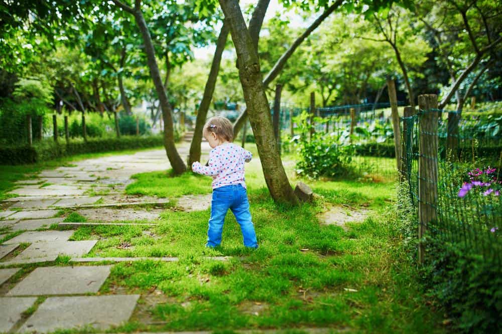 Child exploring a lush green garden with trees and flowers.