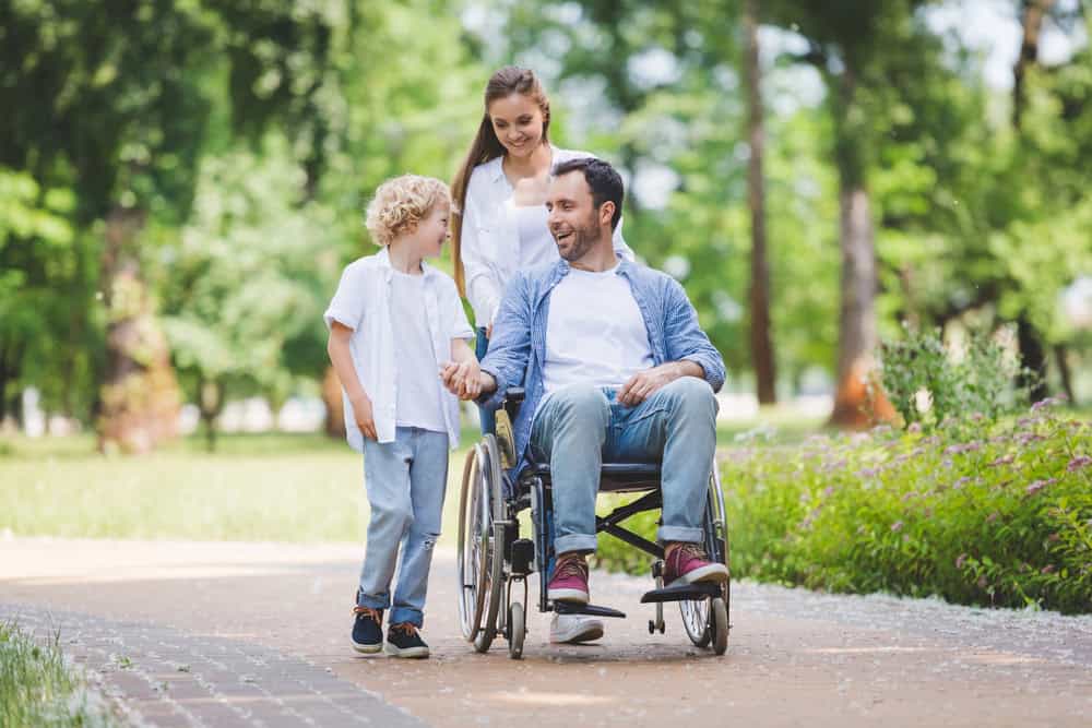 Family enjoying outdoor walk with a man in wheelchair and children in park.