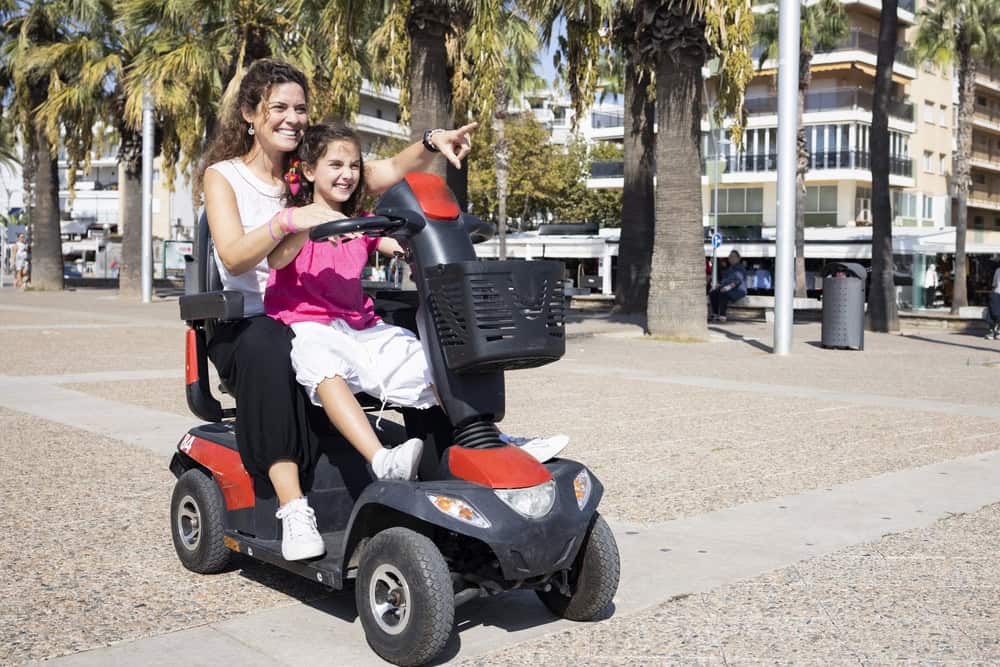 Mother and daughter riding a mobility scooter in a park.