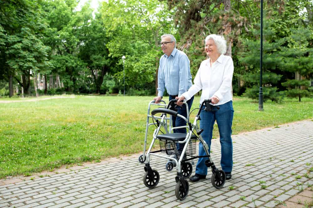 Elderly couple walking outdoors with a walker in a park setting.