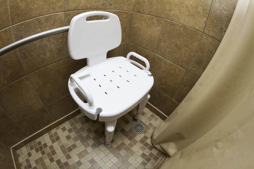 Shower chair with armrests in a bathroom corner for post-surgery mobility aid.