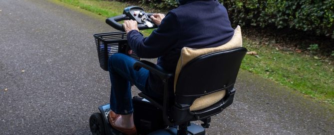 Senior Woman Using A Mobility Scooter Outdoors On A Paved Path.