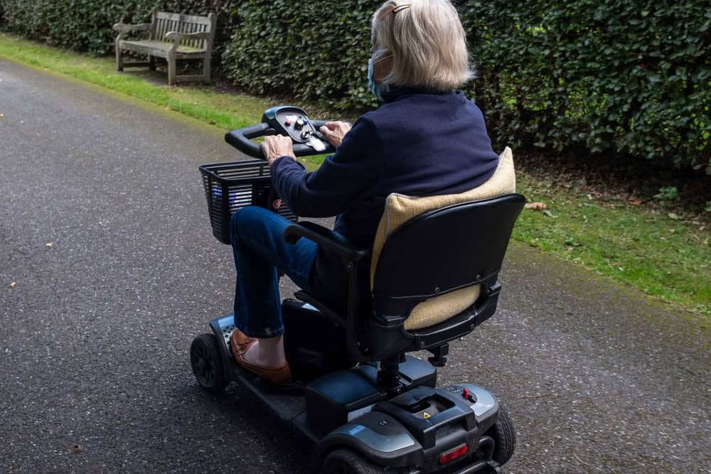 Senior woman using a mobility scooter outdoors on a paved path.