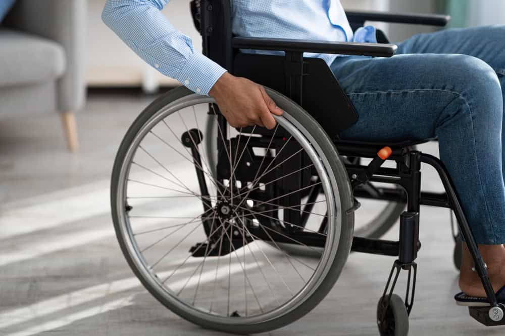 Person in wheelchair indoors, holding wheel with hand, home setting.
