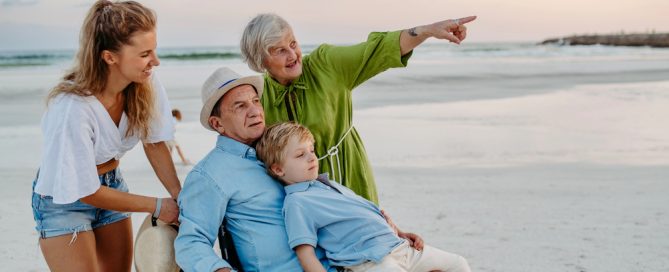 Family At The Beach With A Senior Woman Pointing Towards The Horizon.