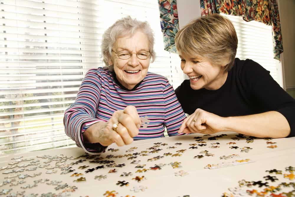 Elderly woman and caregiver solving a puzzle together at home.
