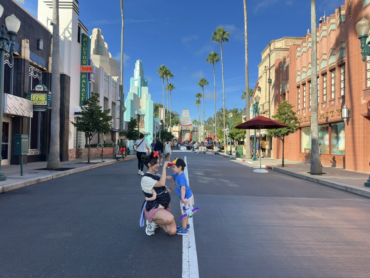 A Mom Carrying Her Baby Kneels Beside Her Toddler On Hollywood Boulevard At Disney'S Hollywood Studios During A Disney World Trip With A Baby And Toddler.