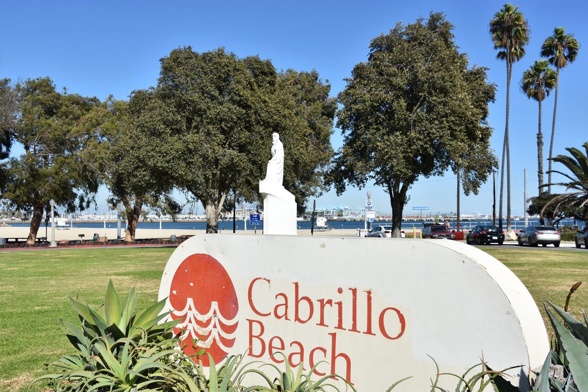 The Cabrillo Beach Sign On A Sunny Lawn With The Harbor And Beach Behind It
